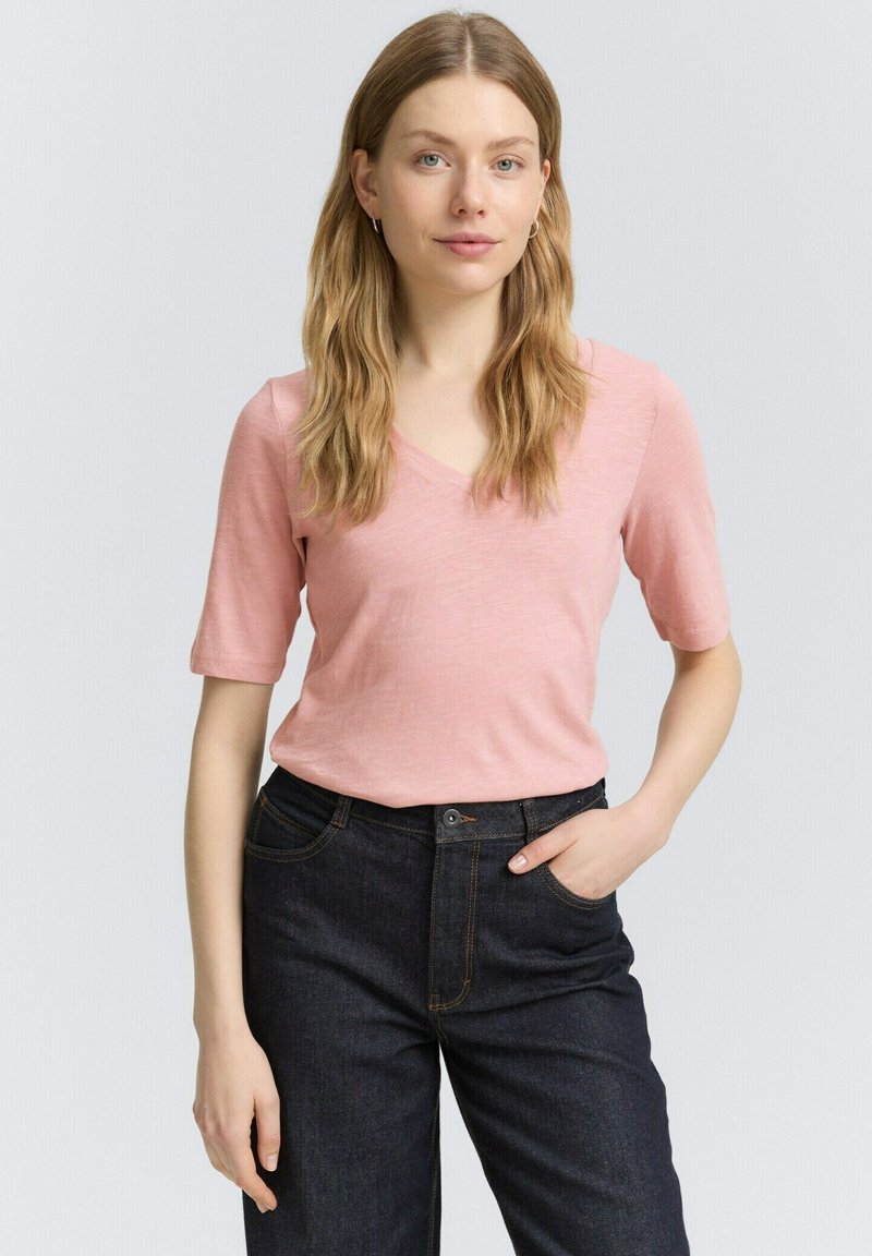 Tricou cu mânecă scurtă, de culoare roz deschis, cu decolteu în V, asortat cu blugi din denim de culoare bleu închis, având o croială lejeră și o textură subtilă a materialului.