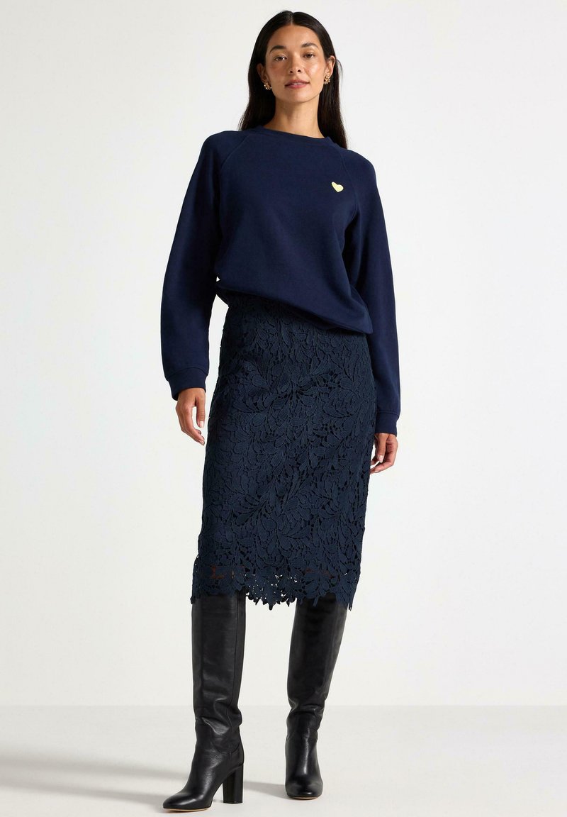 Marineblå sweatshirt med et lille hjertepåsyet, parret med en marineblå blondetop pencil skirt og sorte knelange læderstøvler.