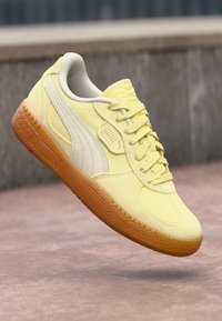 Gule semsket sneaker med hvite detaljer, teksturert gummisåle og flate lisser. Har et Puma-logo på siden og et rundt logomerk.