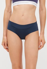 Chilot de bikini bleu marin dintr-un material neted și elastic, cu croială înaltă și acoperire minimă. Dispune de un tiv elastic cu logo.