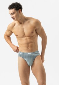 Muskelstarker Mann, der blaue und weiße gestreifte Unterhosen anpasst, steht vor einem schlichten weißen Hintergrund.