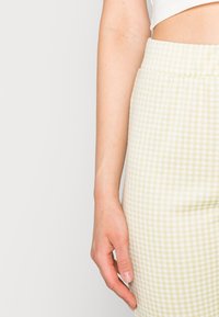 Calças de padrão gingham em tecido amarelo suave e branco com uma cintura elástica, apresentando um acabamento texturizado e silhueta ajustada.