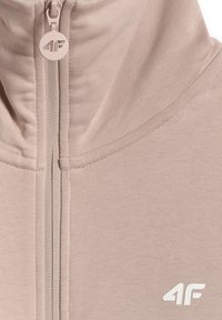 Sweat à capuche beige zippé avec logo 4F sur la tirette de la fermeture éclair et sur la poitrine, avec un col montant et une texture de tissu douce.
