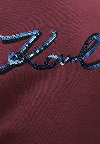 Testo in corsivo blu e nero in paillettes su fondo borgogna che scrive "Amore" con un effetto ombra.