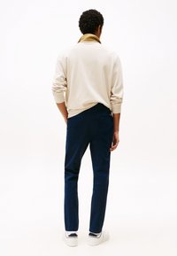 Beige overhemd met lange mouwen en een omgeslagen kraag, gecombineerd met marineblauwe chinos. Witte sneakers met zichtbare zwarte accenten.