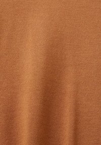 Gros plan sur la texture d'un tissu tricoté marron clair avec de légers plis verticaux et des détails de couture fine.