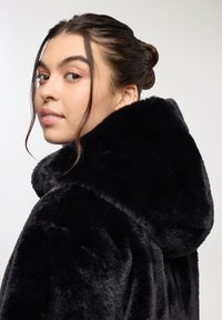 Czarny płaszcz z sztucznego futra z dużym kapturem, miękka tekstura i luźny krój, z gładką powierzchnią i zaokrąglonym kołnierzem.