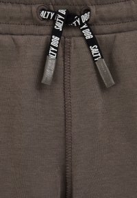 Prim-plan cu material tricotat maro și șnur negru pe care este inscripționat textul „SALTY DOG” în alb, cu o cusătură verticală brodată în centru.