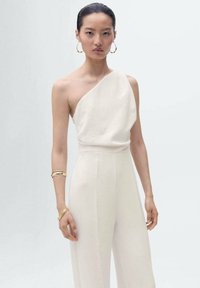 Vit, enaxlad jumpsuit i lätt tyg med draperad design. Har en figursydd midja och vid benlösning. Guldarmband.