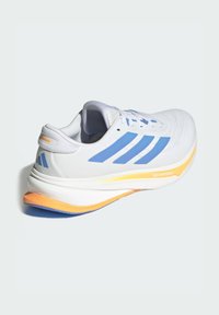 Zapatilla de correr blanca y azul claro con acentos en la suela naranja y "DREAMSTRIKE+" impreso en la entresuela, vista desde un ángulo trasero.