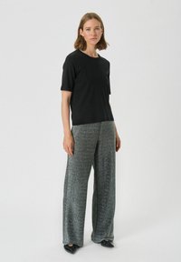 Schwarzes kurzärmliges Oberteil kombiniert mit weiten, glitzernden grauen Hosen. Das Outfit hat eine lockere Passform und eine glatte Textur, ergänzt durch schwarze Schuhe.