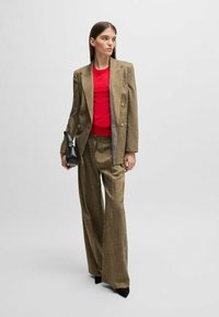 Blazer a righe color crema e pantaloni a palazzo abbinati, indossati con un top rosso aderente e una borsa nera. Silhouette affusolata con rever accentuati.