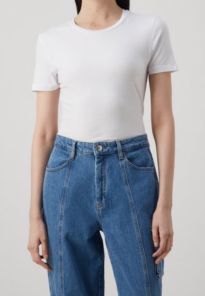 White short-sleeved t-shirt, fitted design, paired with blue high-waisted denim pants featuring front pockets and a button closure.