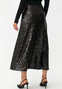Gonna nera in paillettes con una silhouette fluida, lunghezza a metà polpaccio, caratterizzata da una texture liscia e paillettes lucide che riflettono la luce.