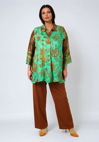 Turquoise blouse with brown sleeves, featuring a floral pattern in gold. Paired with brown wide-leg pants and yellow heels.