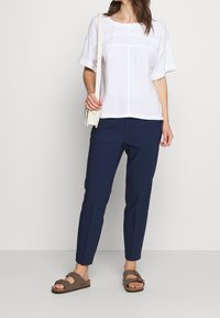 Haut blanc en lin à manches courtes avec une coupe ample, associé à un pantalon slim-fit bleu marine et des sandales marron avec un détail de boucle.
