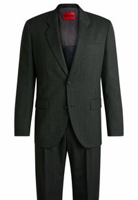 Abito grigio scuro caratterizzato da un tessuto testurizzato, blazer monopetto con due bottoni e pantaloni coordinati. Etichetta rossa HUGO all'interno.