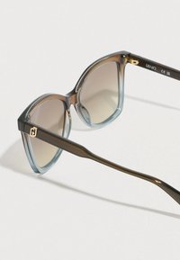 Napszemüveg túlméretezett, macskaszem alakú kerettel barna és kék átmenetes színben. A lencsék barnára színezettek. Arany díszítés található a szárakon.