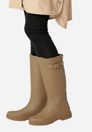 Botas de lluvia altas de goma en color beige con acabado mate, que cuentan con un detalle de hebilla en el lateral y una suela texturizada para más agarre.