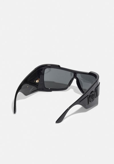 Sorte solbriller med en robust konstruktion, vinklede stel, mørkt tonede linser, mat overflade og en tekstureret detalje på siden.