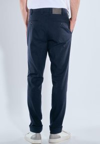 Navy blue trousers made of cotton with a straight cut, featuring two back pockets and a rolled hem, paired with white sneakers.