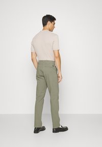 Helles beiges Strickshirt mit kurzen Ärmeln, kombiniert mit olivgrünen geraden Hosen und schwarzen Schuhen. Einfache, klare Linien und minimale Details.