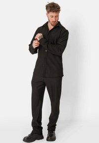 Zwarte lange mouw button-up shirt met een geribbelde textuur in combinatie met bijpassende zwarte broeken. Schoenen zijn chunky zwarte sneakers.