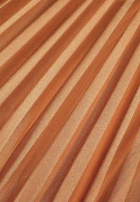 Tissu plissé dans une teinte orange chaude avec des accents métalliques. Surface texturée avec des bandes alternant mat et brillant. Doux et flexible.