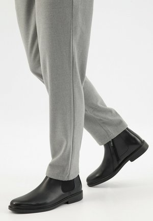 Zwarte leren enkellaarzen met een rits aan de zijkant, een gladde textuur, ronde neus en een stevige zool, gecombineerd met lichtgrijze op maat gemaakte trousers.