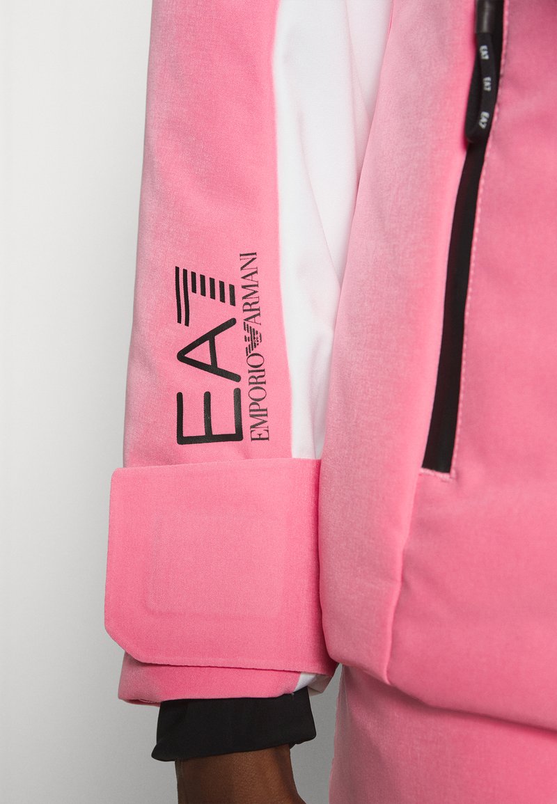 Roze velours jack met een zwart logo op de mouw, contrasterende witte panelen en een stevige manchet met een textuurafwerking.