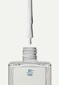 Bottiglia di vetro trasparente con forma rettangolare e un'etichetta bianca che mostra "80 +" e "100". Un liquido bianco gocciola da un contagocce a punta.