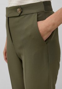Spodnie w oliwkowej zieleni o gładkiej fakturze, wyposażone w zapinanie na guzik, boczne kieszenie oraz dopasowany krój, podkreślone subtelnie teksturowanym paskiem w talii.