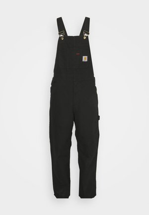 Salopette en coton noir avec bretelles réglables, une poche avant avec un patch logo, et deux poches latérales, offrant une coupe décontractée.