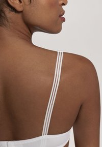 Bela bralette z nežnimi nastavljivimi trakovi, ki se ponaša z gladko teksturo in minimalističnim dizajnom, poudarjajočim čist in moden estetski videz.