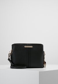 Svart syntetisk crossbody-väska med en mjuk yta, utrustad med detaljer i guldton och en sidrem, dekorerad med två vertikala sömmar.