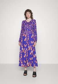 Vestido de mangas compridas, até ao chão, em um vibrante roxo com padrões florais em laranja e azul. Tecido suave com detalhe de decote franzido.