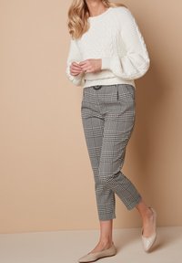 Witte kabelgebreide sweater, zwart-wit geblokte cropped broek, beige ballerina's. Gladde textuur en aansluitend ontwerp.