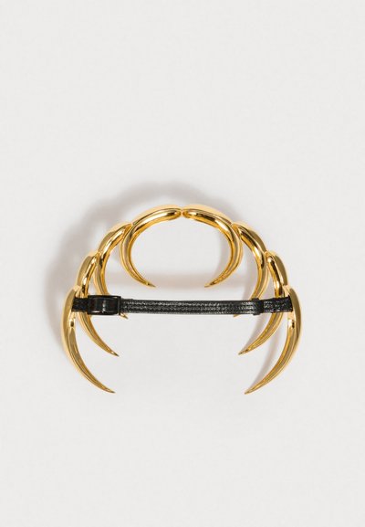 Χρυσόχρωμος κλιπ μαλλιών σε σχήμα νύχτας με πέντε καμπύλες οδοντωτές άκρες. Διαθέτει μαύρη δερμάτινη λωρίδα για ασφαλές κλείσιμο. Απαλή υφή και γυαλιστερή εμφάνιση.