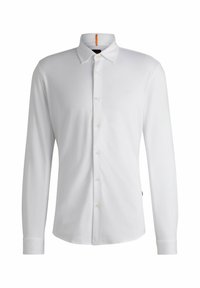 Chemise blanche à manches longues en coton doux, avec un col boutonné, un devant à boutonnières et un petit logo sur la poitrine.