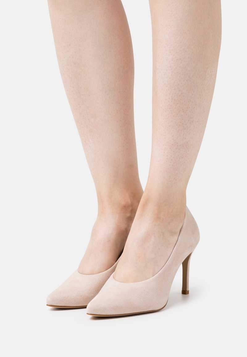 Escarpins en daim beige avec un bout pointu et un talon aiguille fin. Texture lisse et design simple ; aucune décoration visible.
