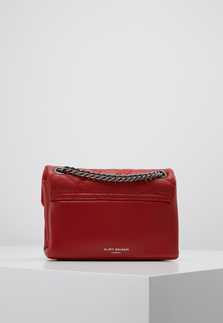 Czerwona pikowana skórzana torebka z srebrnym łańcuszkiem i wytłoczonym logo z przodu, o gładkiej fakturze i kompaktowym prostokątnym kształcie.
