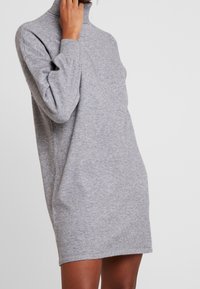 Robe turtleneck en tricot gris avec des manches longues, une coupe décontractée, longueur mi-cuisse et texture douce. Design minimaliste sans motifs.