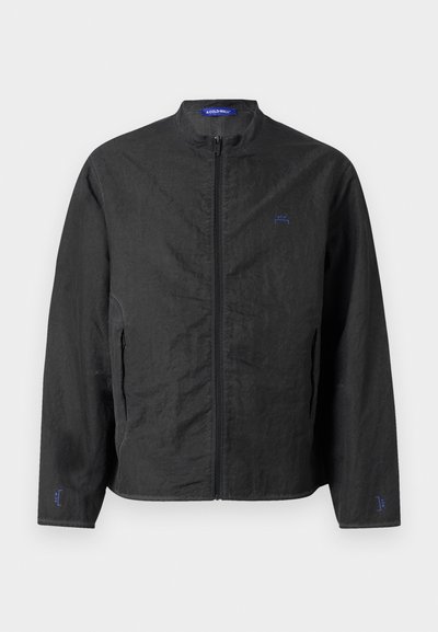 Chaqueta ligera negra con cuello alto, cremallera frontal y puños elásticos. Presenta un pequeño logo azul en el pecho y una tela texturizada.