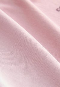 Hele roosa kangas, millel on sile tekstuur ja peen kudumismuster, voltitud, et näidata selle pehmust ja õrna läiget.