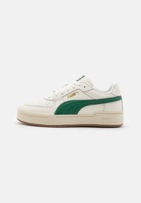 Baskets basses blanches Puma avec une bande latérale verte, semelle beige, avant perforé et logo Puma doré sur le côté.