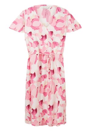 Femme portant une robe rose et blanche à motifs longueur genou avec manches courtes et sandales plates beige, debout sur fond blanc.