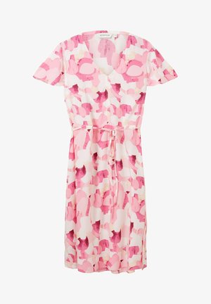 Femme portant une robe rose et blanche à motifs longueur genou avec manches courtes et sandales plates beige, debout sur fond blanc.