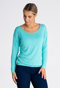 Turkusowa bluzka z długim rękawem o szerokim dekolcie i miękkiej fakturze, w połączeniu z ciemnoniebieskimi, dopasowanymi dżinsami.