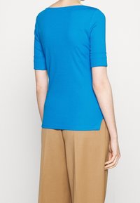 Top azul ajustado de manga corta con un escote amplio y aberturas laterales, combinado con pantalones beige de cintura alta. Tejido suave y elástico.