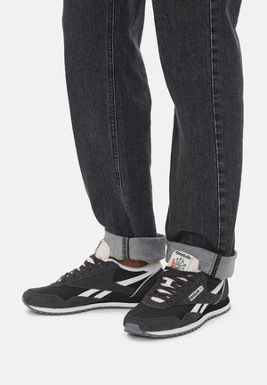 Czarno-szare buty sportowe z białymi akcentami, tekstylną cholewką, wyściełanym kołnierzem i gumową podeszwą, zestawione z ciemnymi dżinsami ze zwiniętymi mankietami.